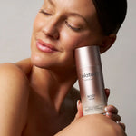 Woman holding a 'plated' body serum bottle against a neutral background